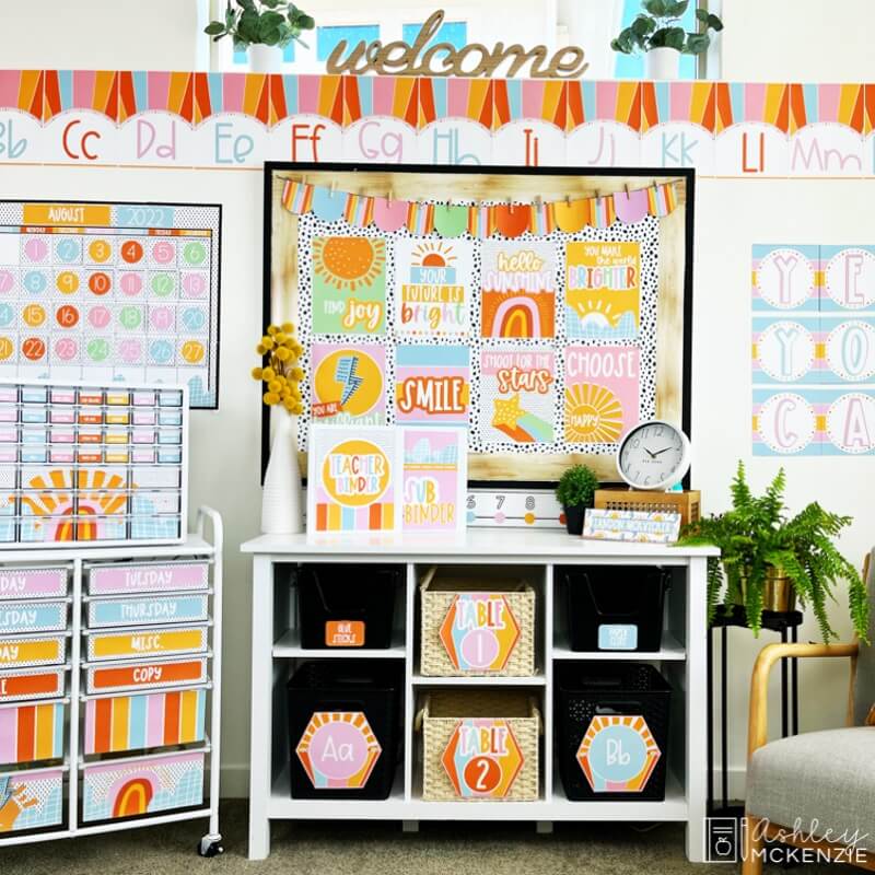 A classroom completely decorated in a cheerful sunshine decor theme. Brightly colored alphabet posters border the room, while a vibrant bulletin board display features sunshine posters with a variety of inspiring sayings.