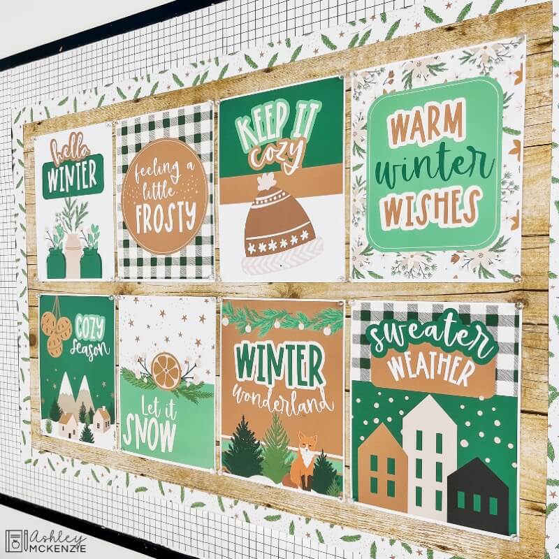 Modern Winter classroom posters featuring eight unique designs are displayed on a bulletin board. Sayings like "hello winter," "keep it cozy," and "warm winter wishes" are shown.