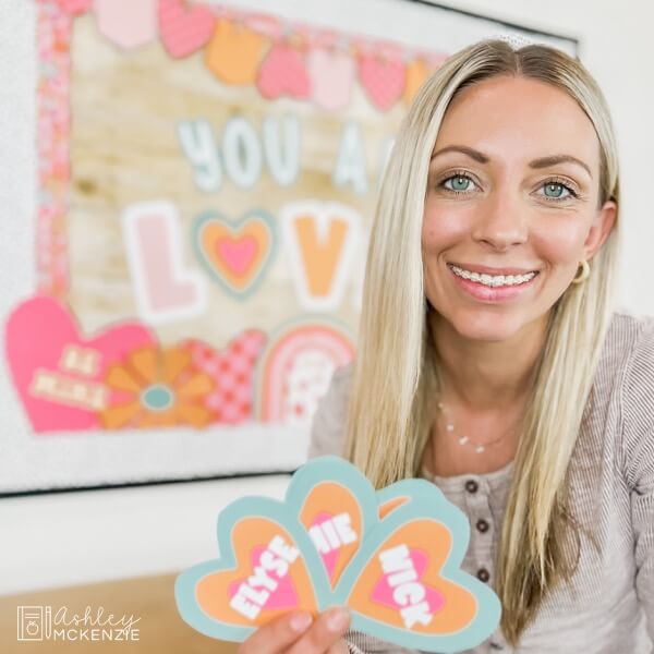 Colorful hearts are held up that each feature a students' name to be hung on a classroom Valentine's Day display.