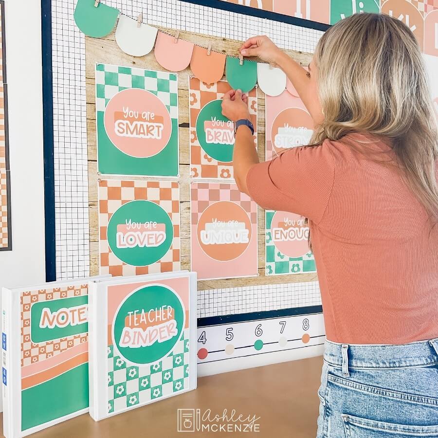 A woman decorating a bulletin board in a modern checkered theme. She's adding banners to a decorated bulletin board display in a classroom.