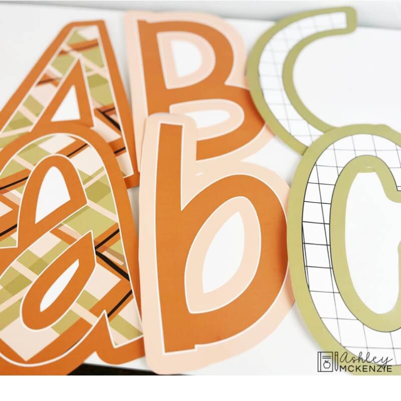 Upper case and lower case "A B C" printed bulletin board letters are shown featuring a neutral browns and greens pattern.