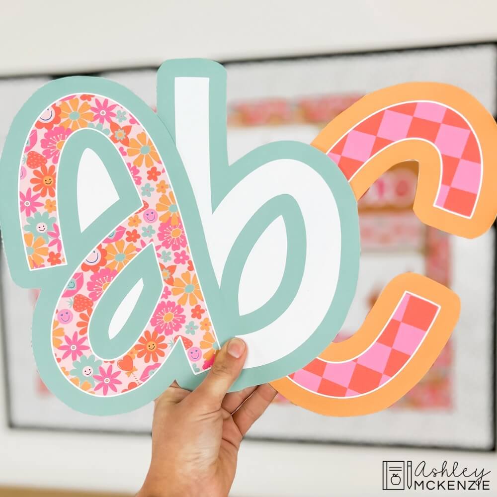 Lower case letters "A B C" are held up featuring a bright Valentine themed color palette and patterns.
