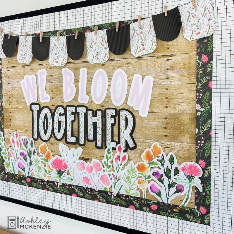 A classroom bulletin board decorated with a wildflowers theme with the saying "We bloom together"